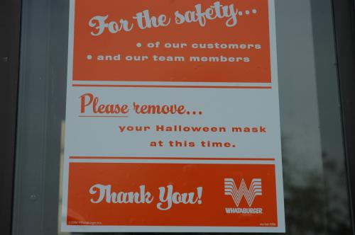 Please Remove Your Mask This photograph zooms in on a white and orange Whataburger sign that reads, "For the safety...of our customers and our team members. Please remove...your Halloween mask at this time. Thank You!"