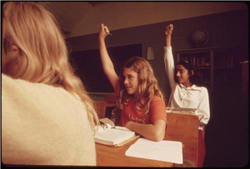 Students Raising Hands Three students sitting at desks with their hands raised